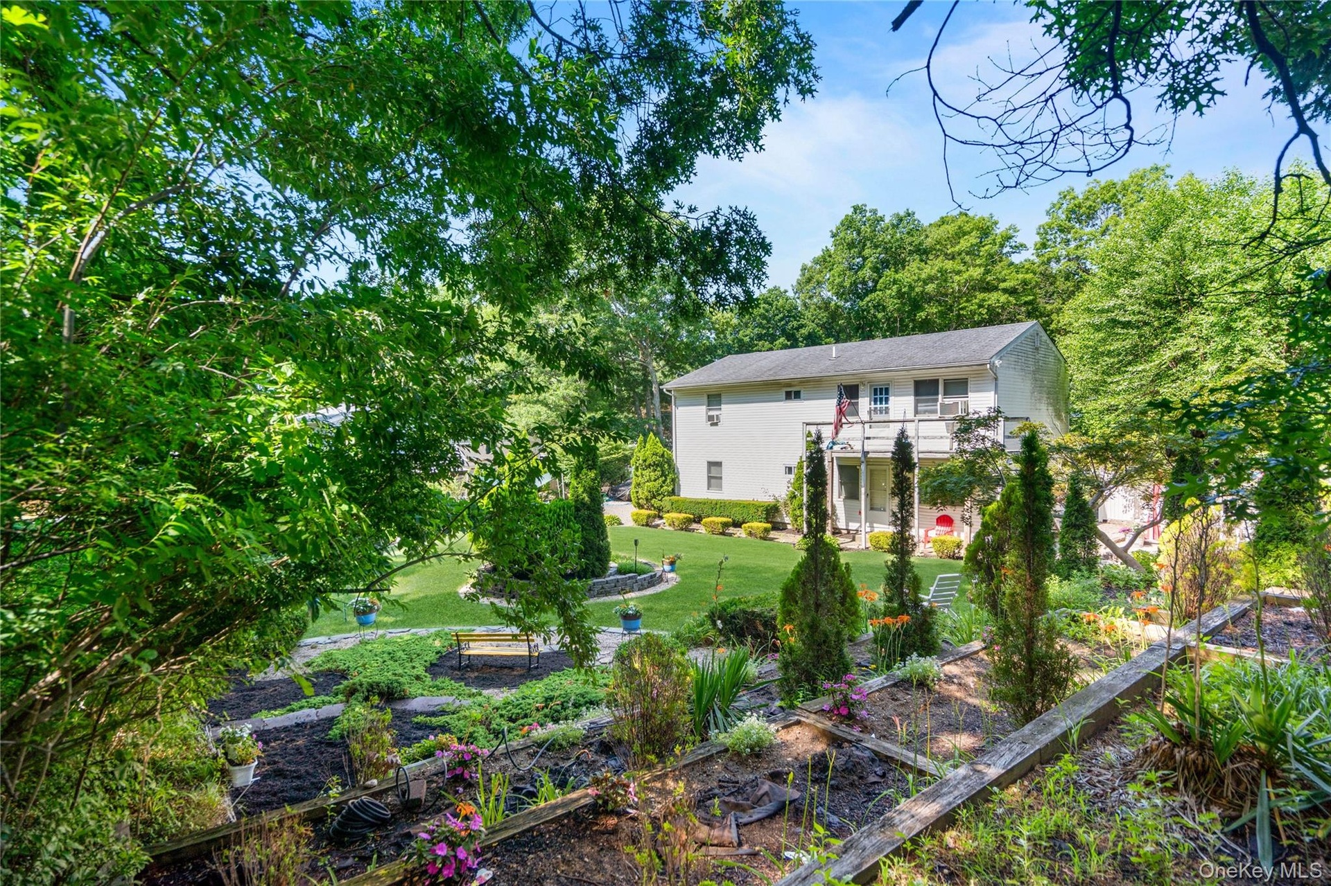 Three-tier terrace garden beds with layered shrubs and a charming park bench create a beautiful, structured outdoor retreat.