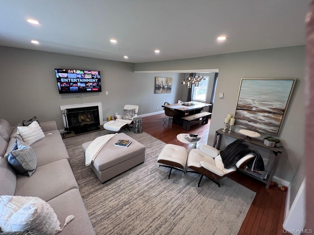 Large living room open floor plan to dining area with recessed lighting, wood-finish flooring, and a wood burning fireplace