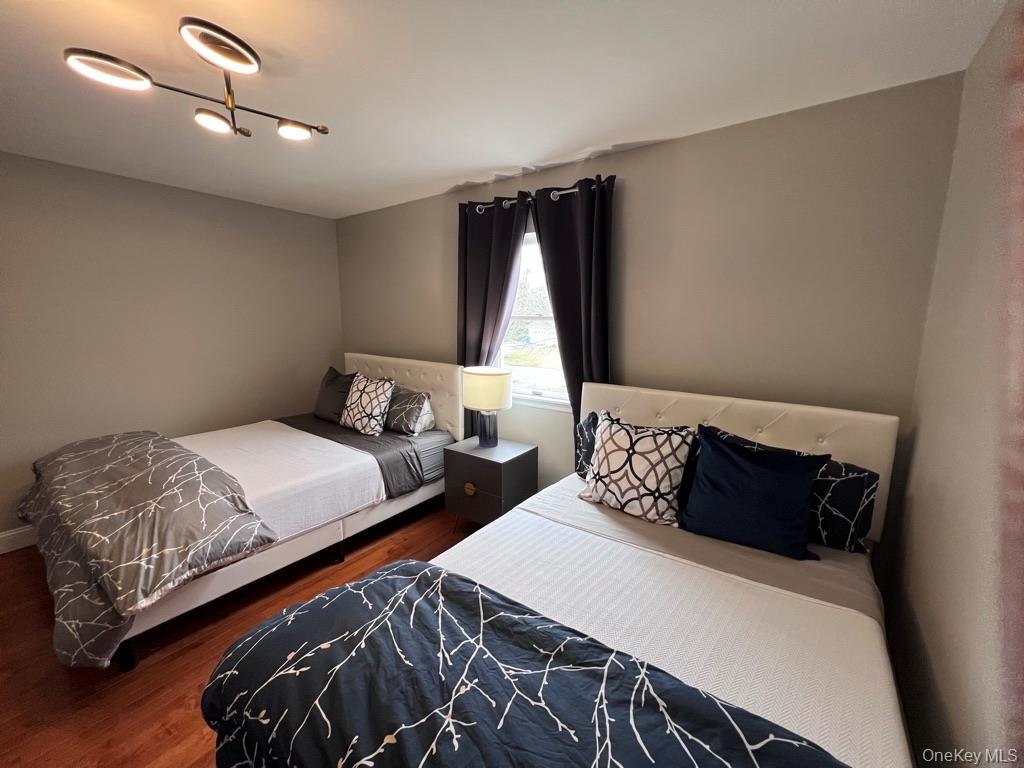 Third bedroom with two full size-beds and wood-finish flooring with neutral wall paint and a modern ceiling light fixture