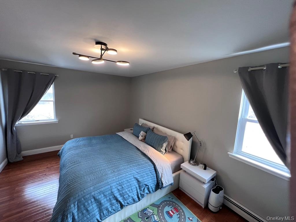 Second bedroom with california-king-size bed and hardwood flooring, light gray wall paint, and a modern ceiling light fixture, two windows allow cross