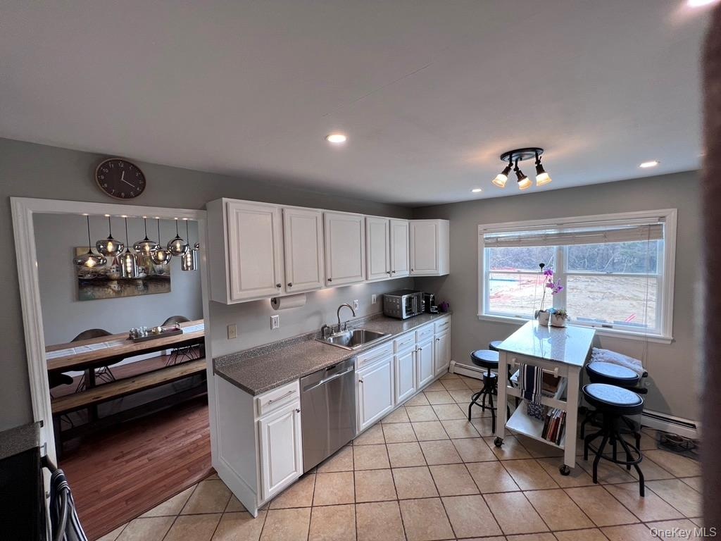 Kitchen featuring white cabinetry, stainless steel dishwasher, tile flooring, recessed lighting, and a large window facing backyard and view of swimmi