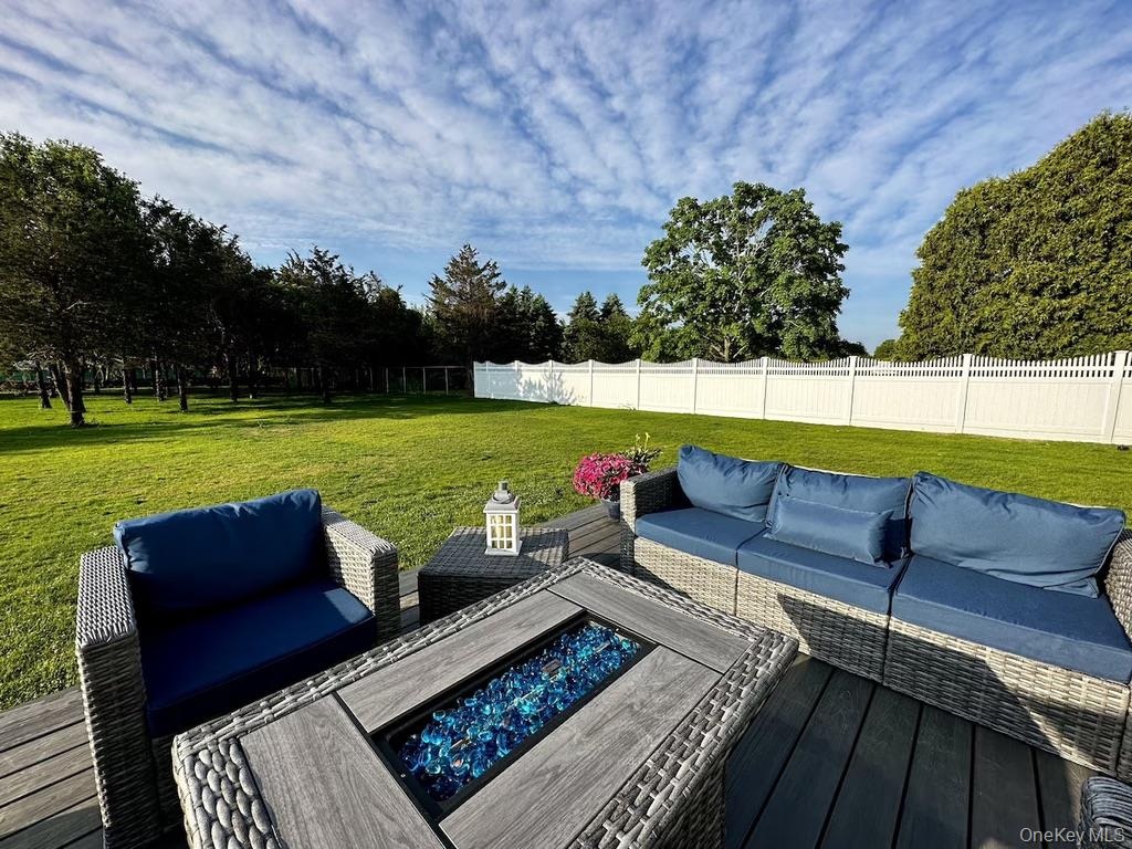 Expansive outdoor decking with a fire pit, overlooking a manicured lawn, mature trees, and a white privacy fence