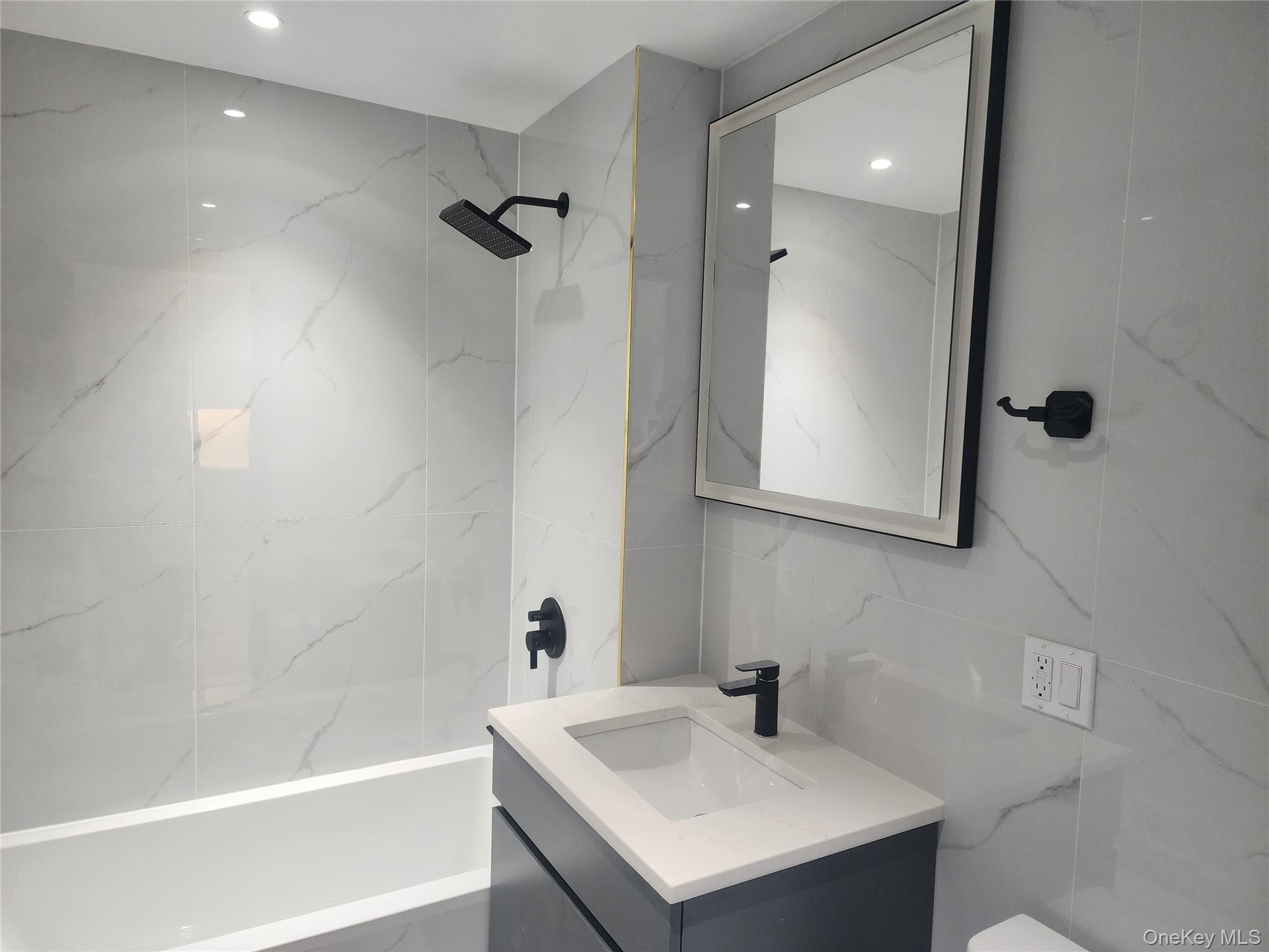 Full-height tiled walls, recessed lighting, matte black fixtures, integrated bathtub, and a floating vanity with a vessel sink