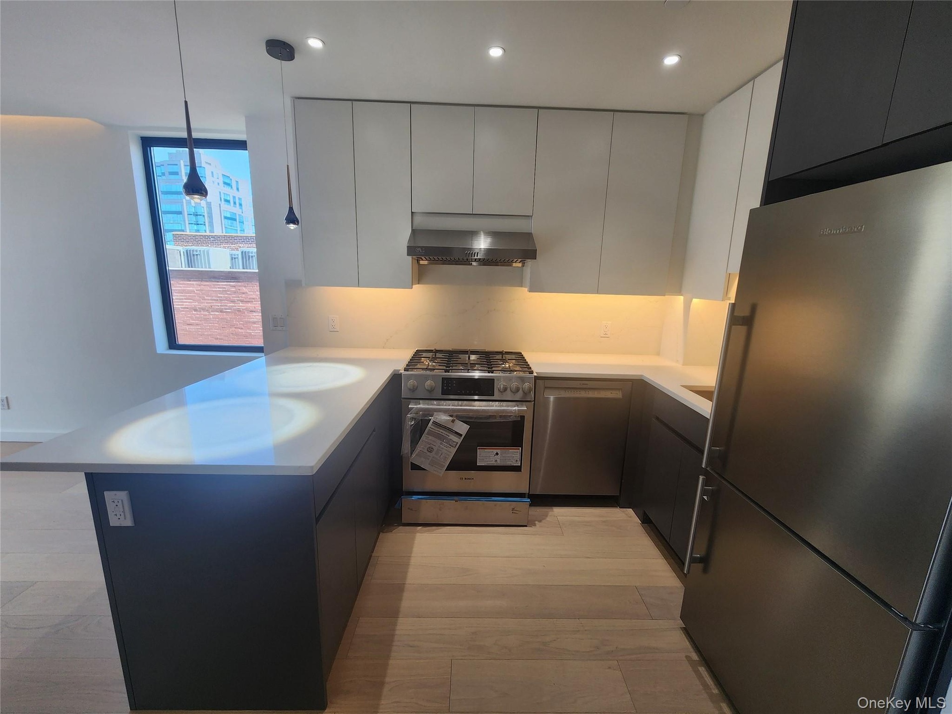 U-shaped kitchen featuring wood-finish flooring, stainless steel appliances, white countertops, dark lower cabinetry, and light upper cabinetry