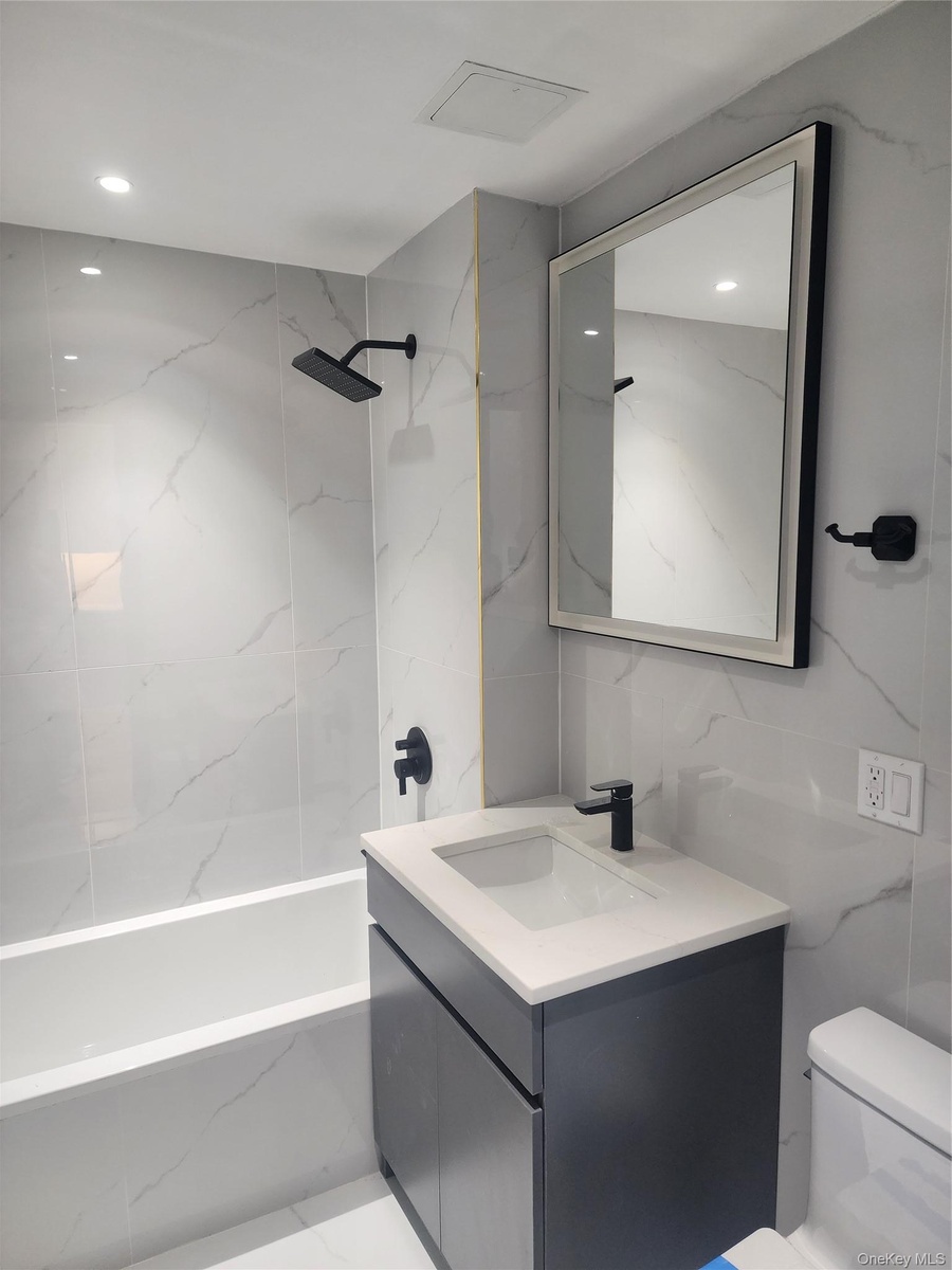 Bathroom featuring a white subway tile bathtub surround, modern black shower fixtures, a dark wood-finish vanity with an integrated sink, a light-colo