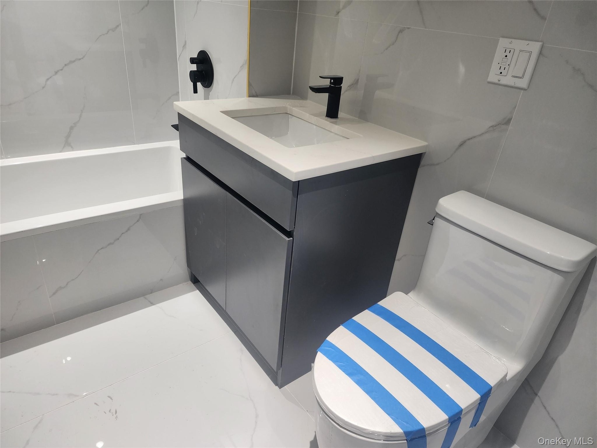 Bathroom featuring a white soaking tub, vanity with a rectangular basin, black faucet, and tiled walls