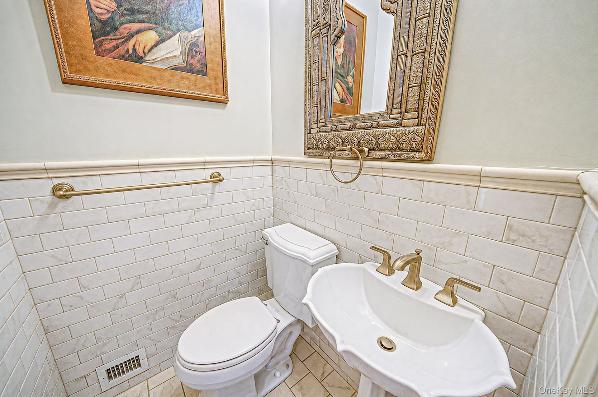 White subway tile wainscoting, pedestal sink with brass-finish fixtures, and decorative mirror