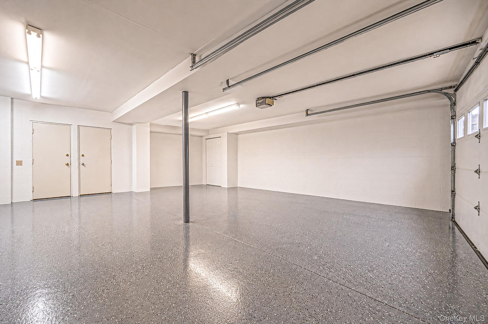 Epoxy-coated flooring, white walls, overhead fluorescent lighting, two panel doors, and a roll-up garage door with windows