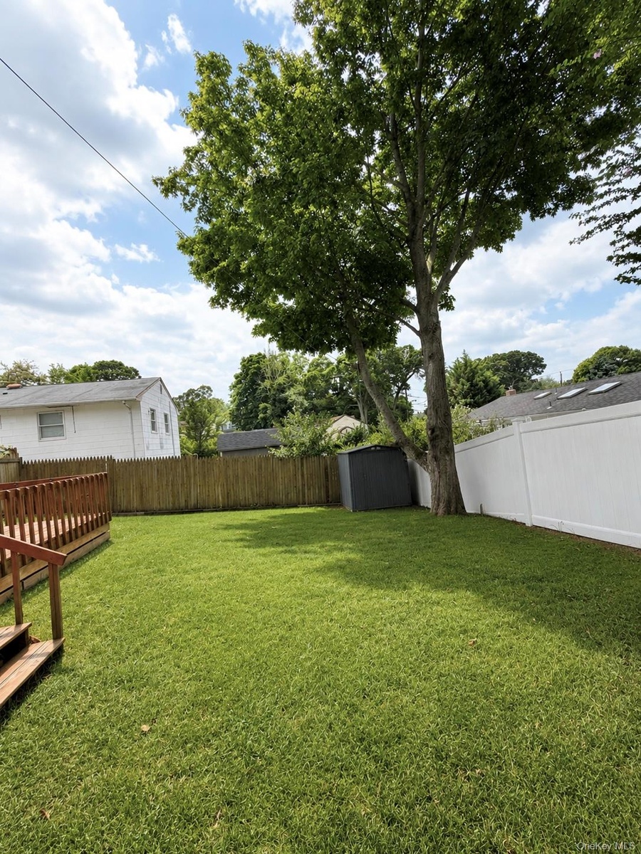 Green lawn, a wooden deck, a privacy fence along the perimeter, and mature trees providing natural shade.