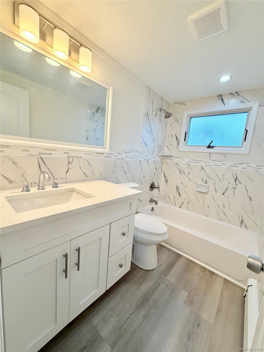 Bathroom featuring a single vanity with stone-finish countertop and  built-in bathtub.