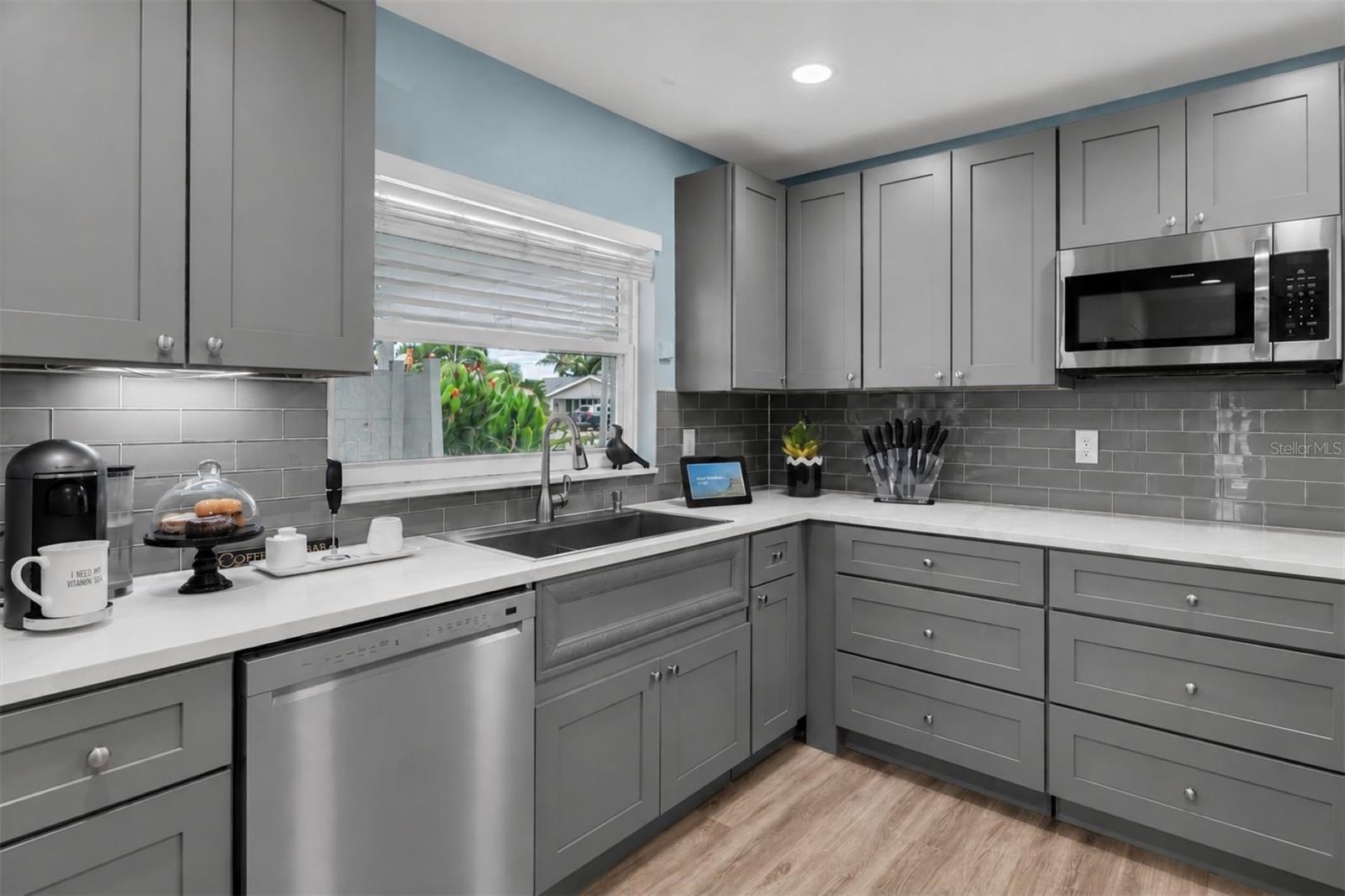 Updated kitchen features gray custom cabinetry with soft-close drawers, quartz countertops and sleek gray tile backsplash.