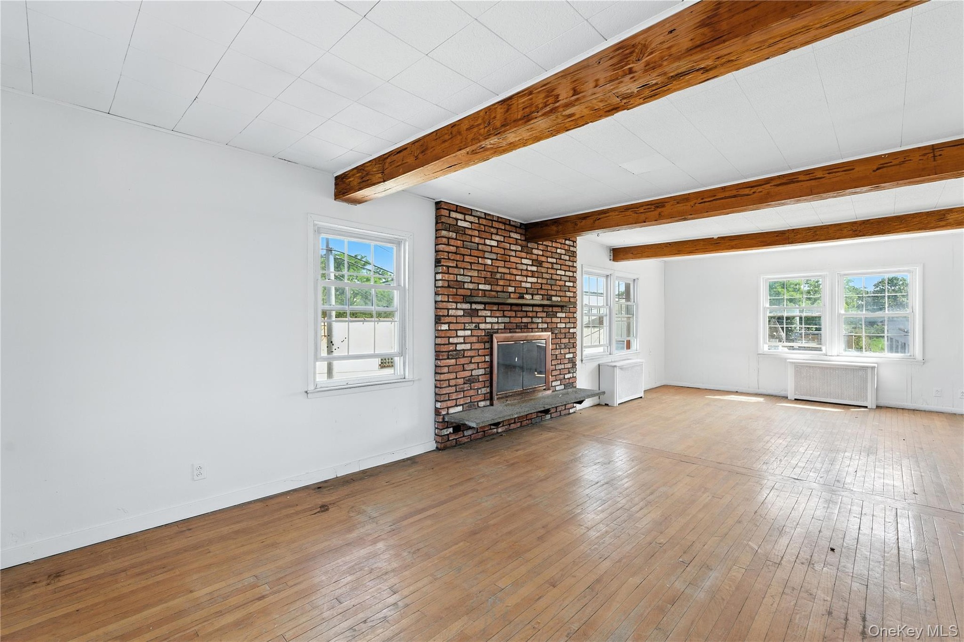 Unfurnished living room featuring hardwood / wood-style floors, radiator heating unit, a brick fireplace, and beam ceiling
