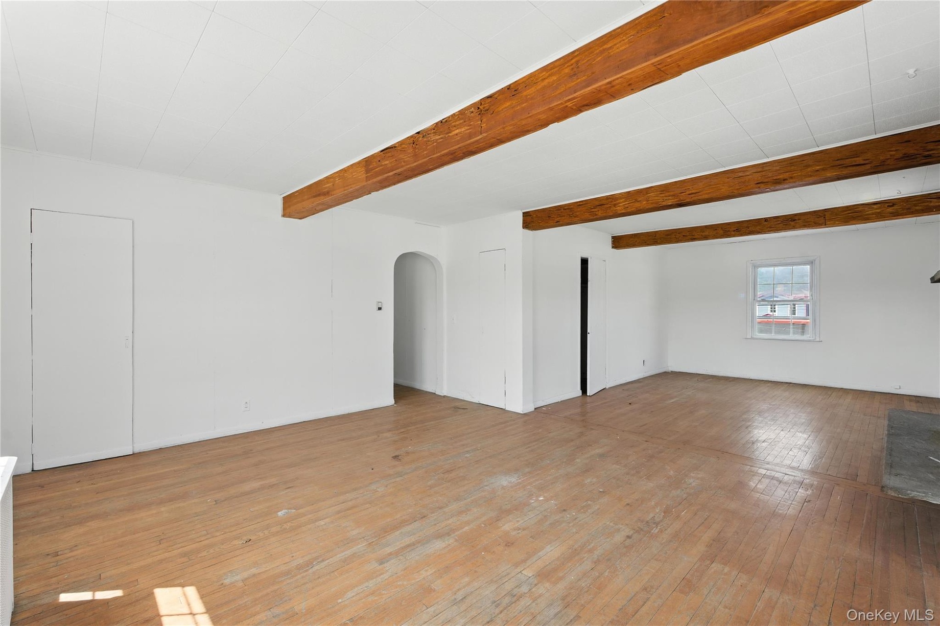 Spare room with light wood-style floors, arched walkways, and beamed ceiling