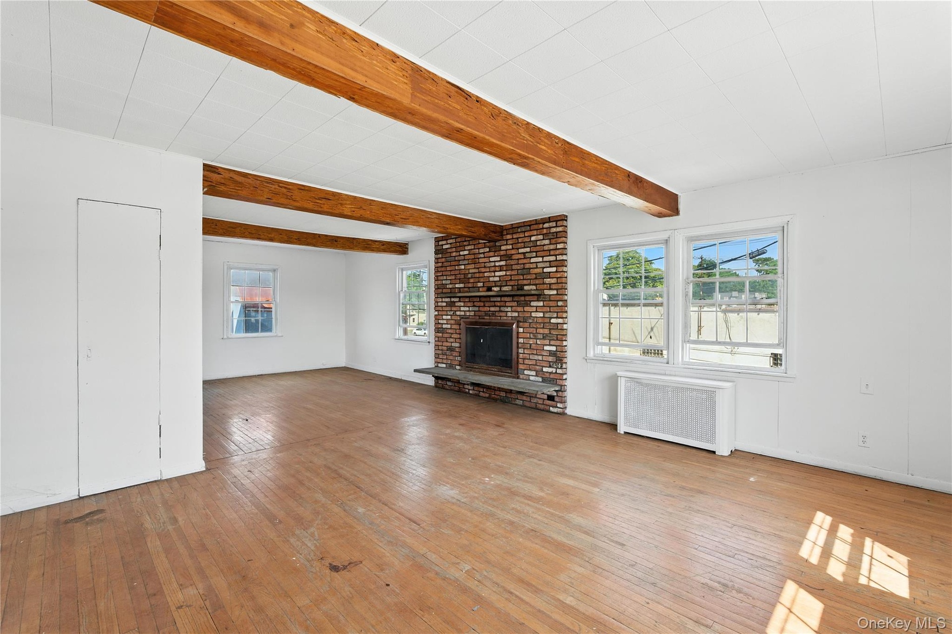 Unfurnished living room featuring light wood finished floors, beamed ceiling, radiator heating unit, and a fireplace