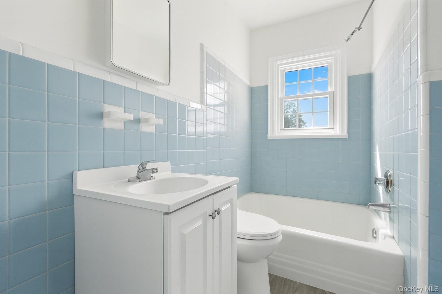 Bathroom with bathing tub / shower combination, tile walls, vanity, and wainscoting