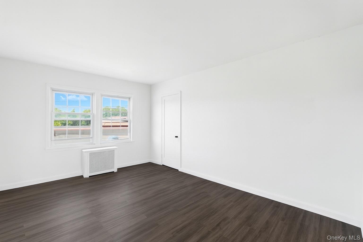 Spare room featuring radiator heating unit and dark wood-type flooring