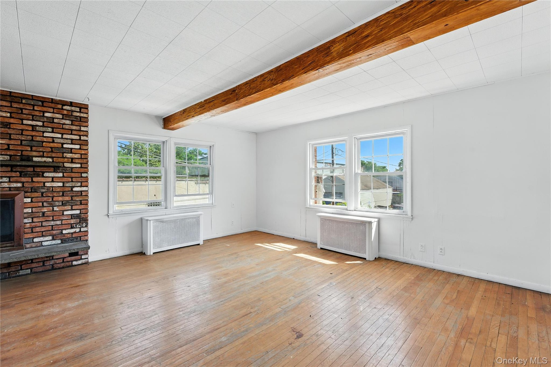 Unfurnished living room featuring light wood-style flooring, radiator, beam ceiling, and a brick fireplace