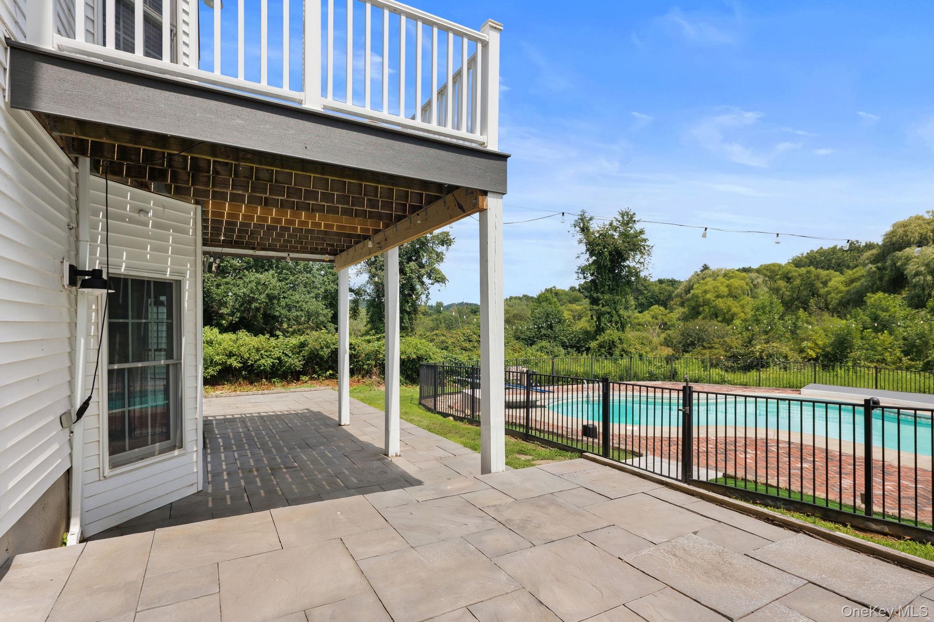 Outdoor patio with large format pavers, adjacent to a fenced in swimming pool with brick decking.