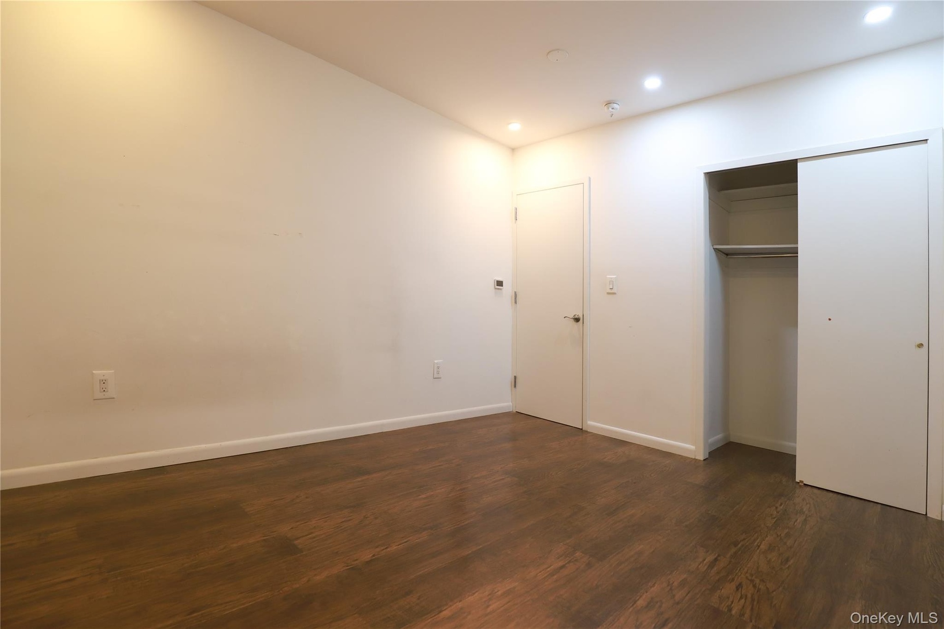 Wood-finish flooring, recessed lighting, white walls, and a built-in closet with sliding doors
