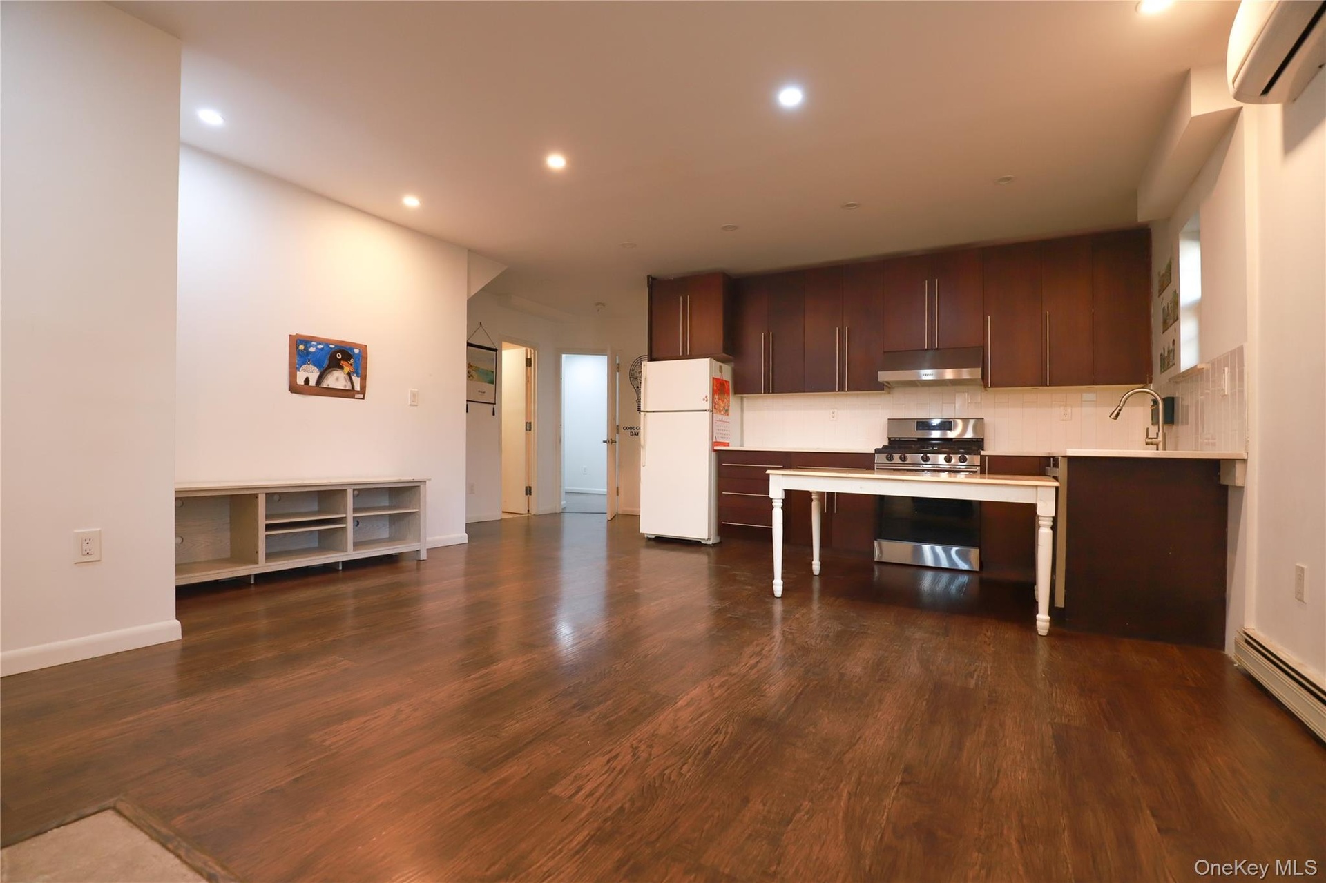 Rich wood-finish flooring throughout, recessed ceiling lighting, kitchen featuring wood cabinetry, stainless steel range and hood, and a white subway 