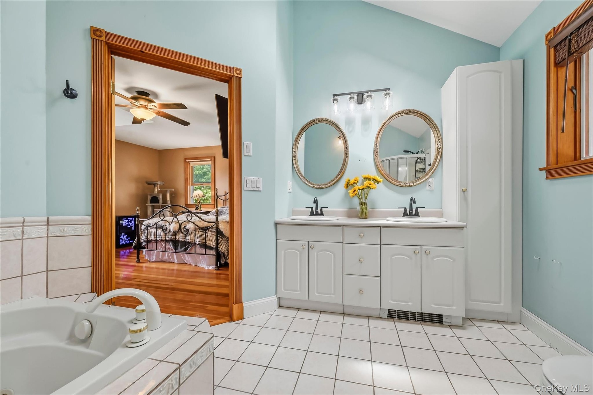 Primary bathroom with double vanity with dual sinks, built-in storage cabinet, tiled flooring, and soaking tub with tiled surround