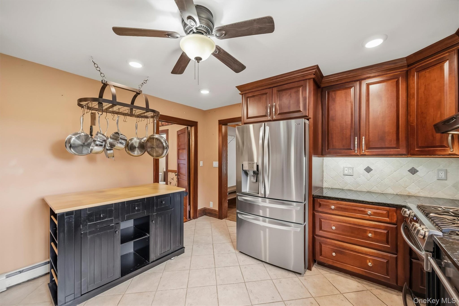 Kitchen with wood cabinetry, stainless steel appliances, tile flooring and additional storage space.