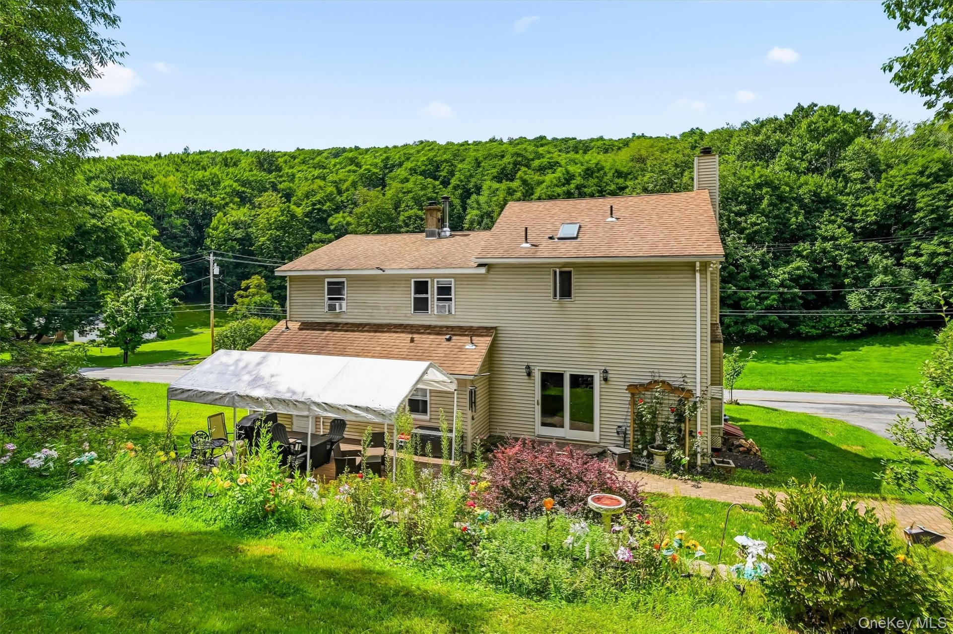 Rear exterior with patio, gardens, and wooded views.