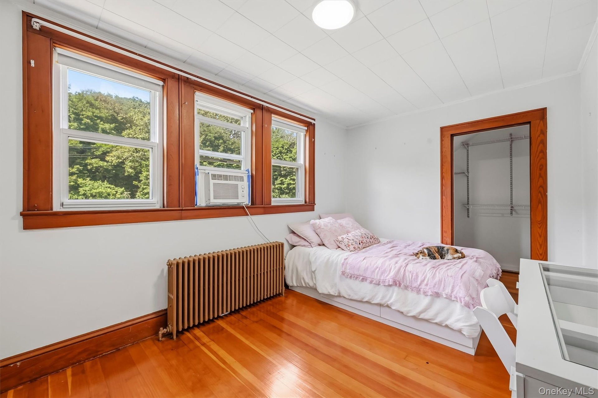 Bedroom with hardwood floors, three windows and generous closet space.