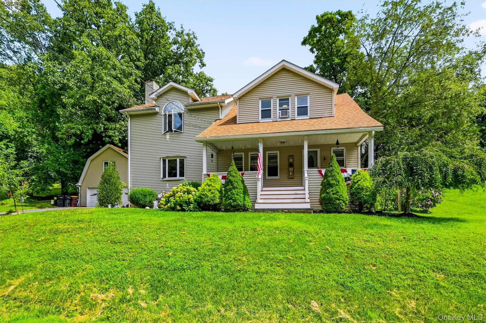 Front exterior featuring a covered porch, spacious lawn and detached garage.