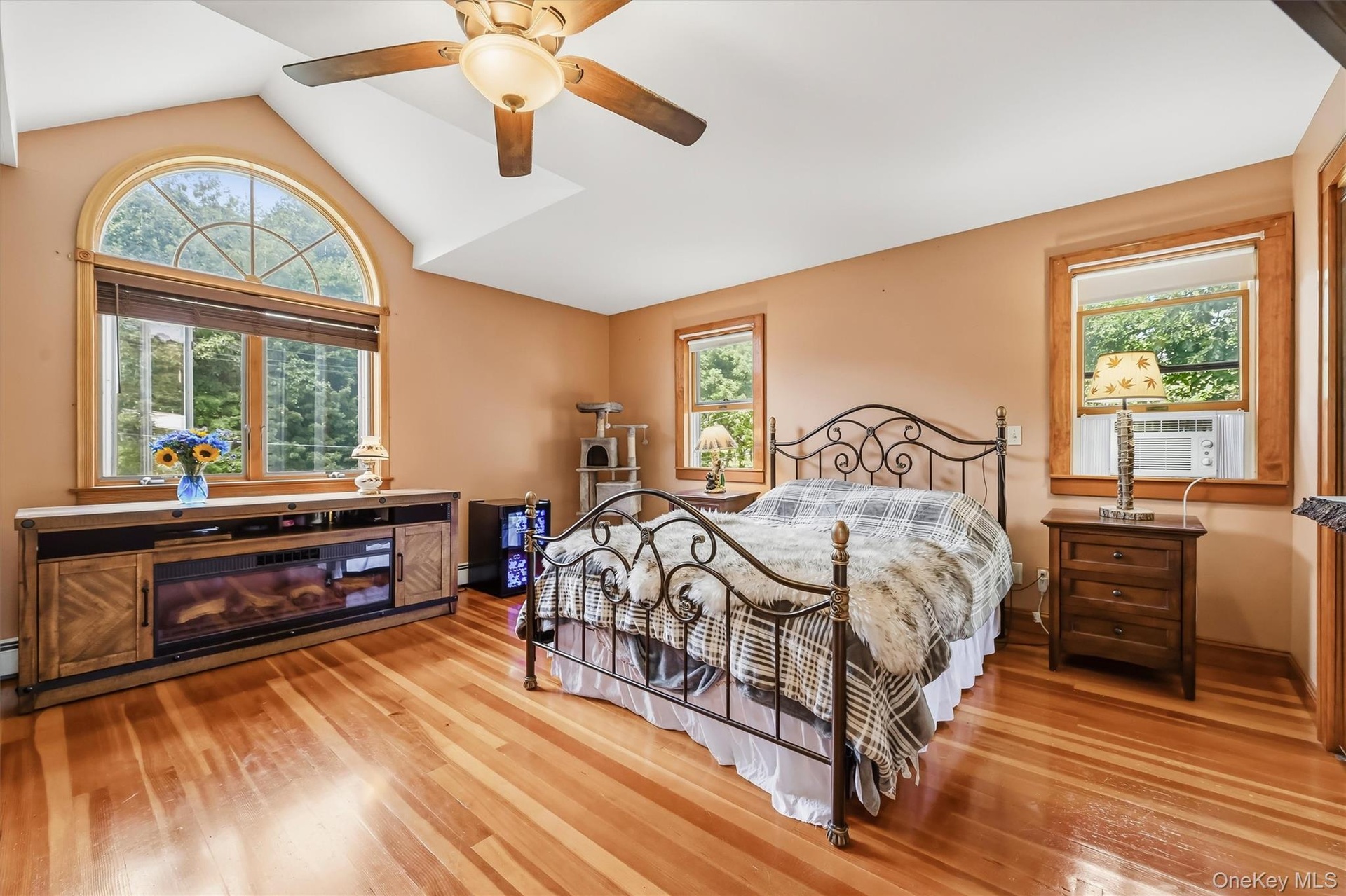 Primary bedroom with hardwood floors, vaulted ceiling and a large arched window.