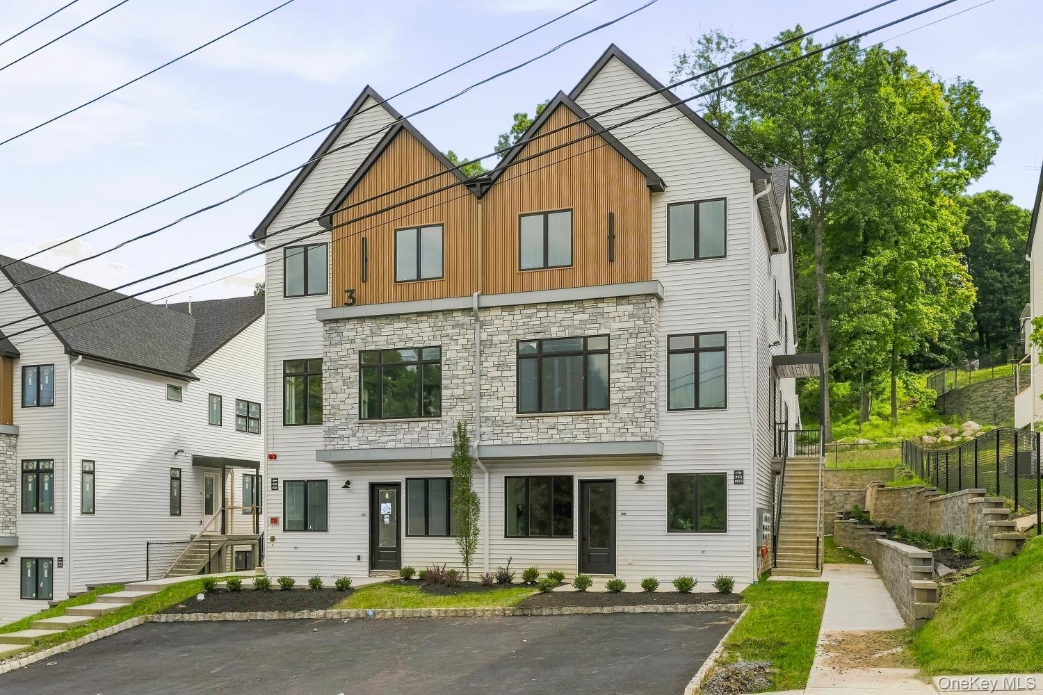 Modern multi-story exterior with white siding, stone accents, and wood-finish paneling