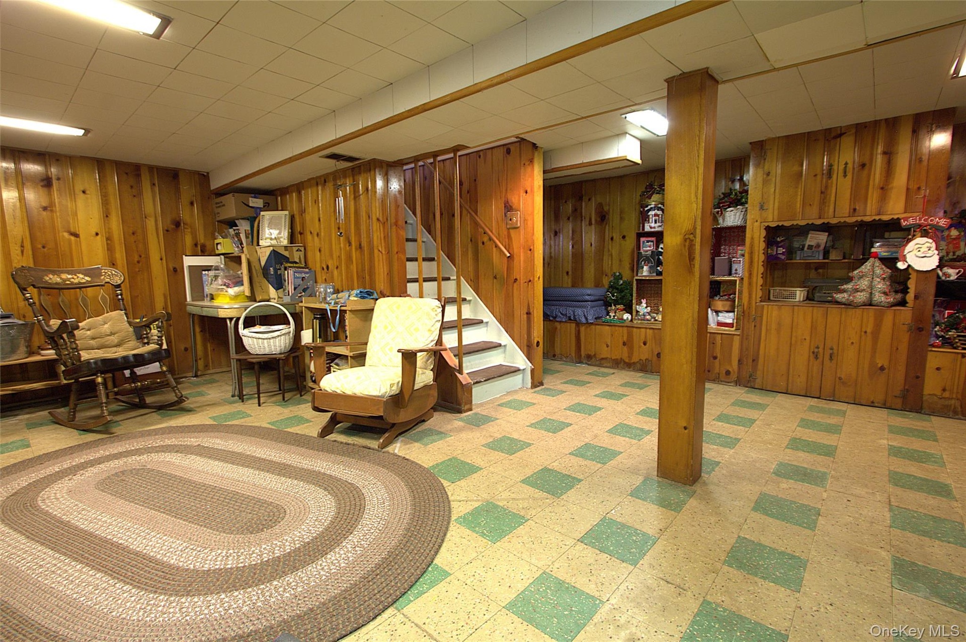 Wood paneling throughout, built-in shelving, staircase with wood railing, recessed panel ceiling, and patterned flooring