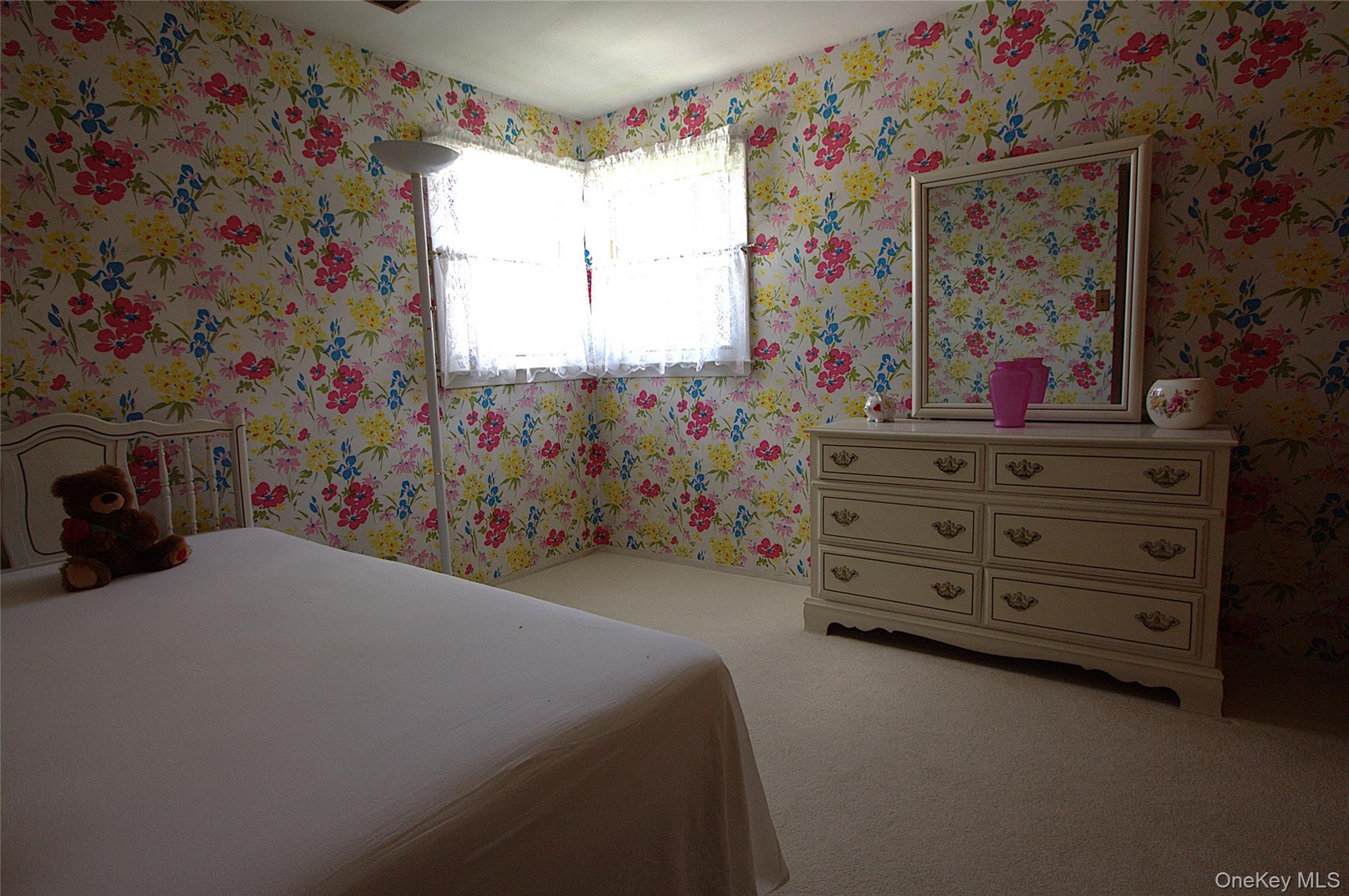 Wallpapered walls featuring a floral pattern, window with white lace curtains, and light-toned carpeting