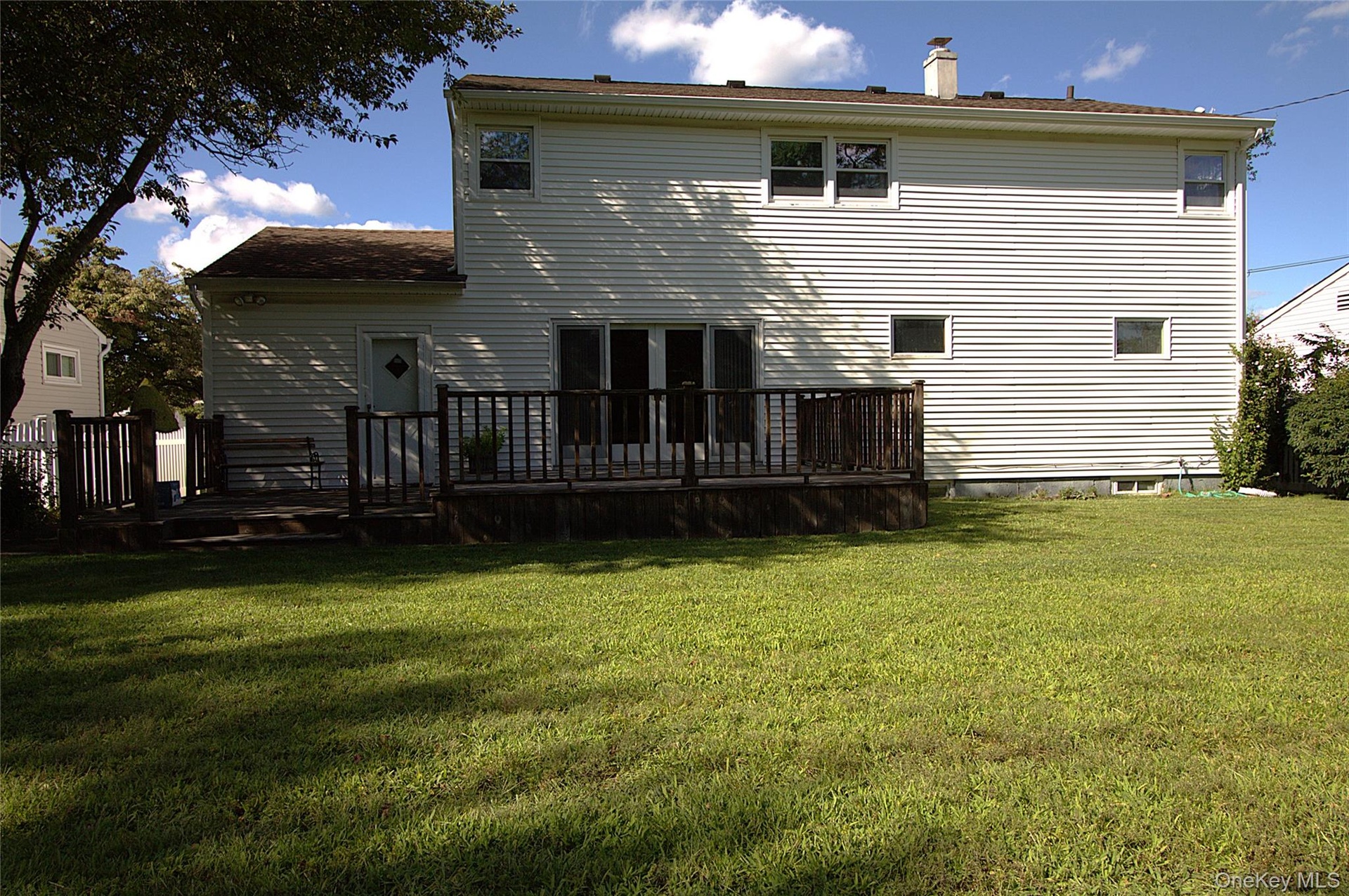 Expansive yard featuring a large wooden deck with railing, white siding, and multiple windows