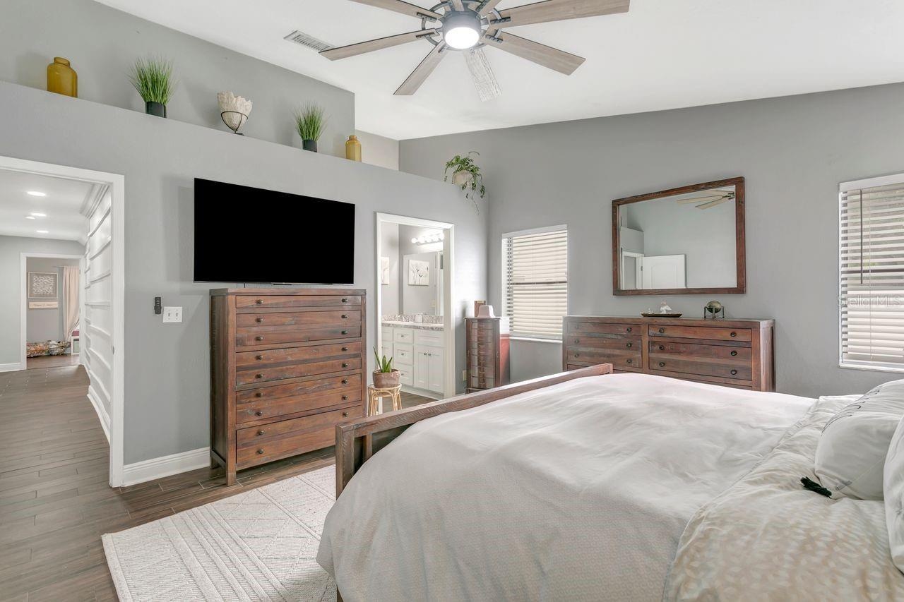 Primary Bedroom with LVP Flooring; Ceiling Fan; Decorative Ledge; En-Suite Bathroom; 2 Closets; and View to Hallway