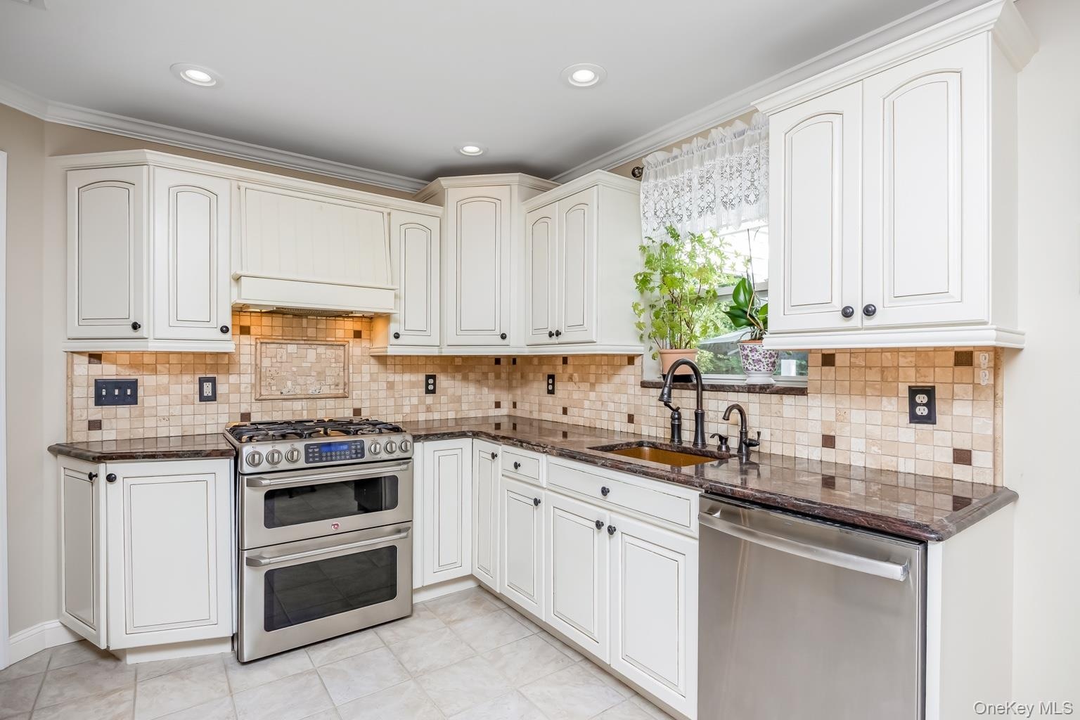 White cabinetry, brown granite countertops, mosaic tile backsplash, stainless steel appliances, and a double oven range