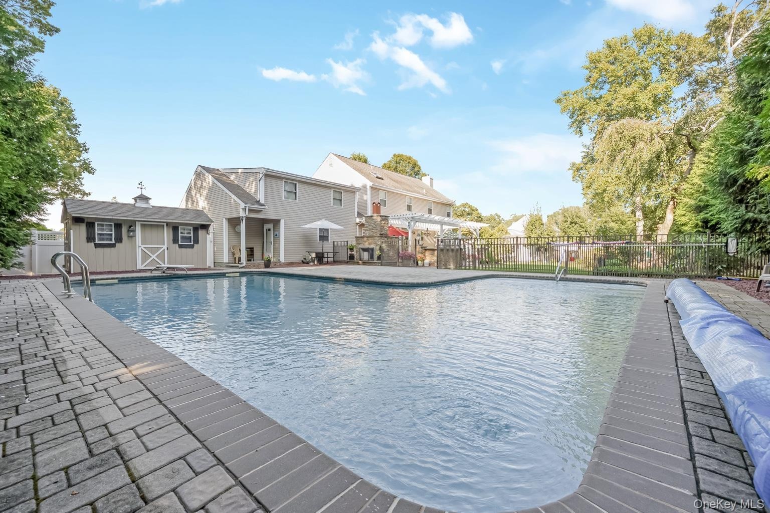 In-ground swimming pool with brick paver surround, accompanied by a detached storage shed