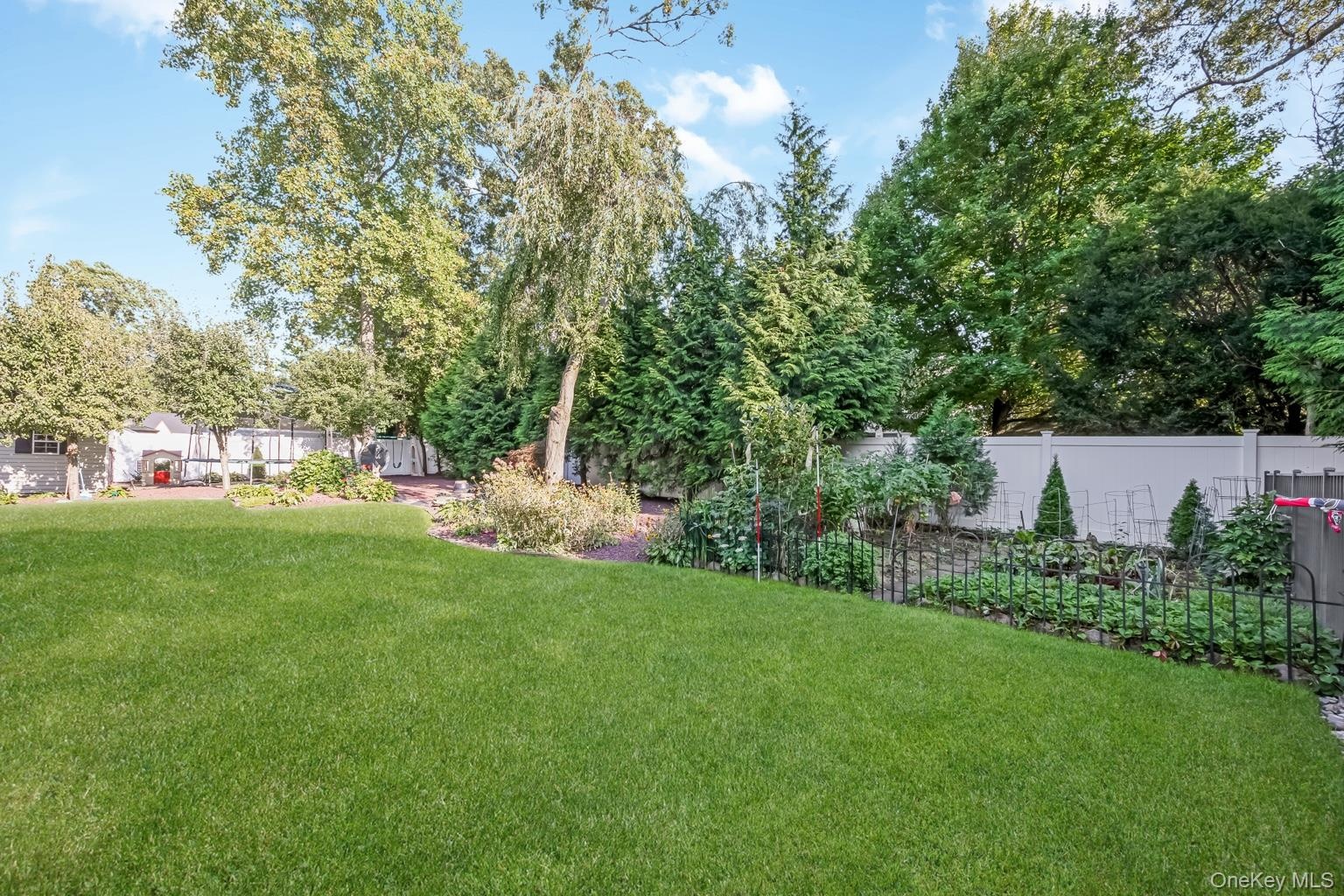 Expansive lawn area with surrounding mature trees, perimeter fencing, and cultivated garden beds