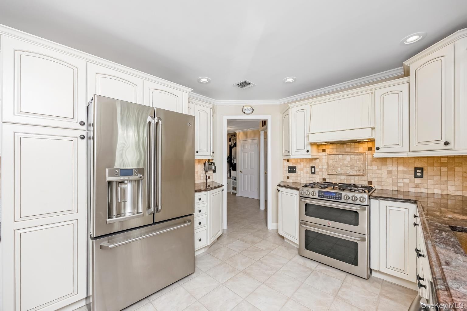 White shaker-style cabinetry, stainless steel French door refrigerator, stainless steel double oven range, mosaic tile backsplash, and light-toned til