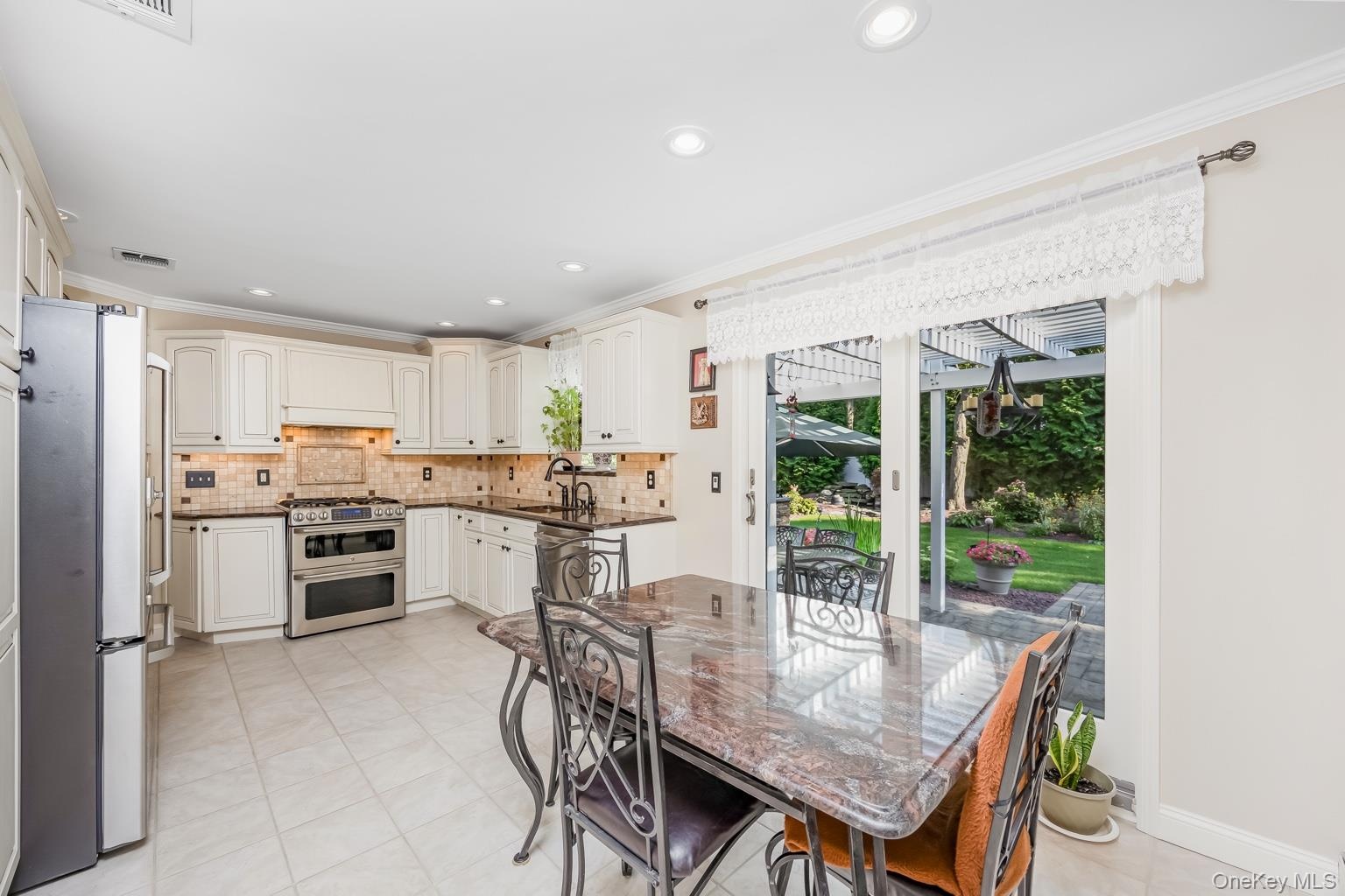 Kitchen featuring white cabinetry, stainless steel appliances, dark countertops, and a tiled backsplash, with sliding glass doors opening to the exter