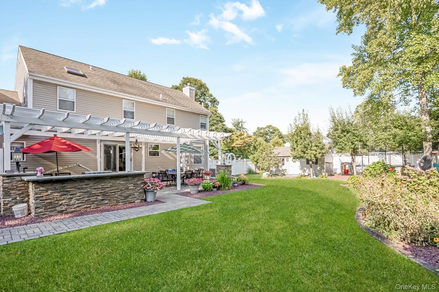 Expansive lawn with a paver patio, stone-faced outdoor kitchen area, and a white pergola structure