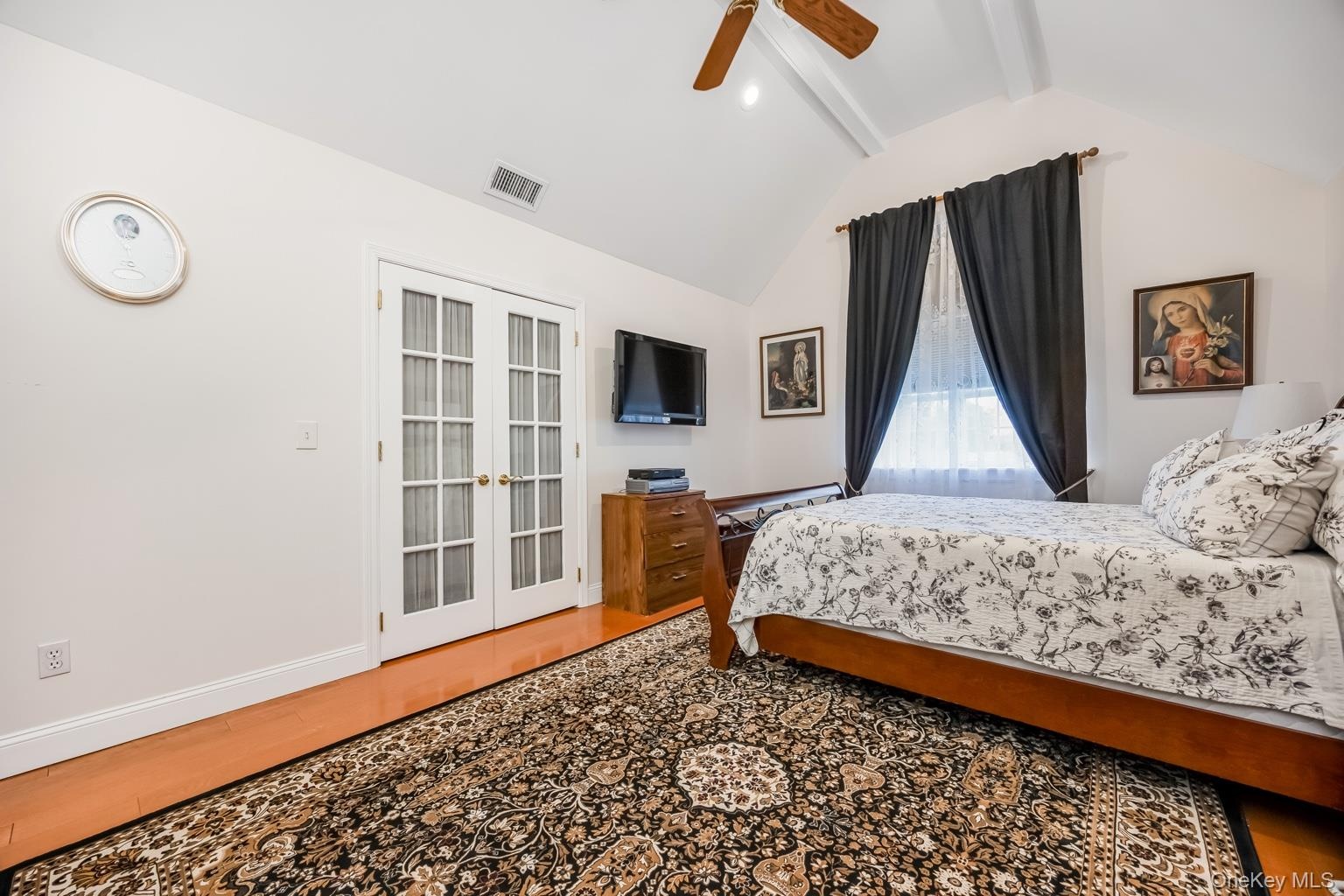 Vaulted ceiling with exposed beams, wood-finish flooring, white French doors, and ceiling fan