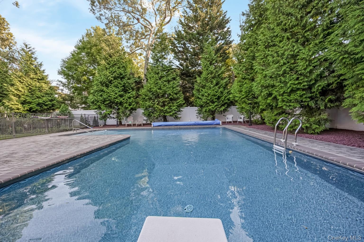 In-ground swimming pool featuring a diving board, surrounding paver patio, and integrated steps