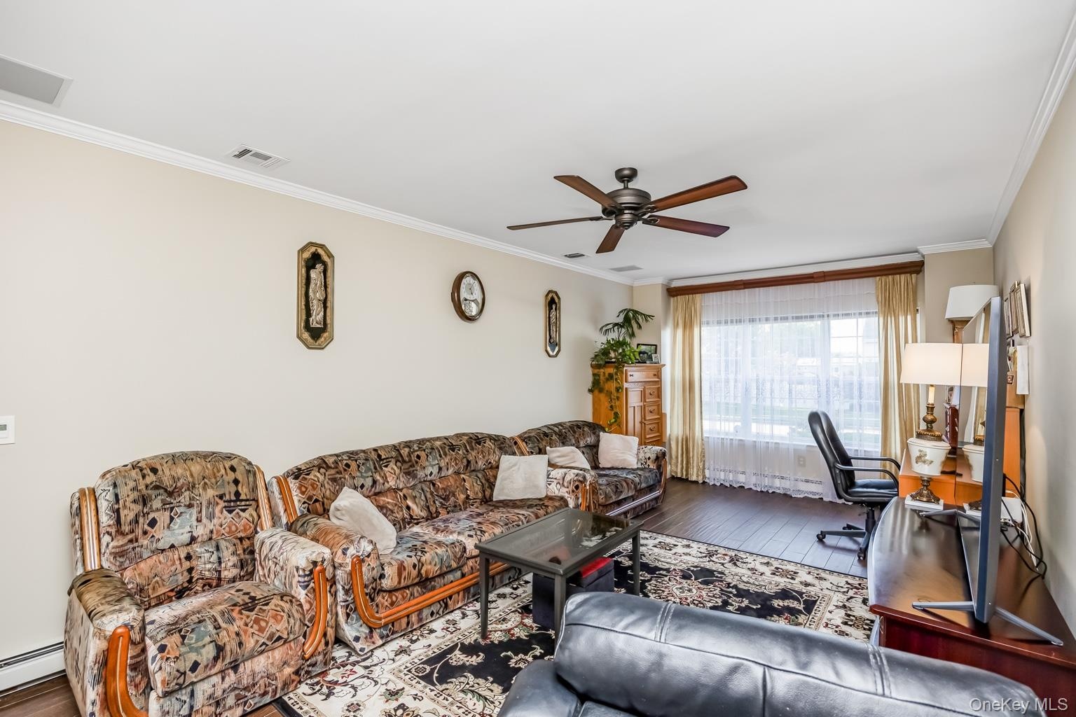 Hardwood-style flooring, crown molding, a ceiling fan, and window treatments