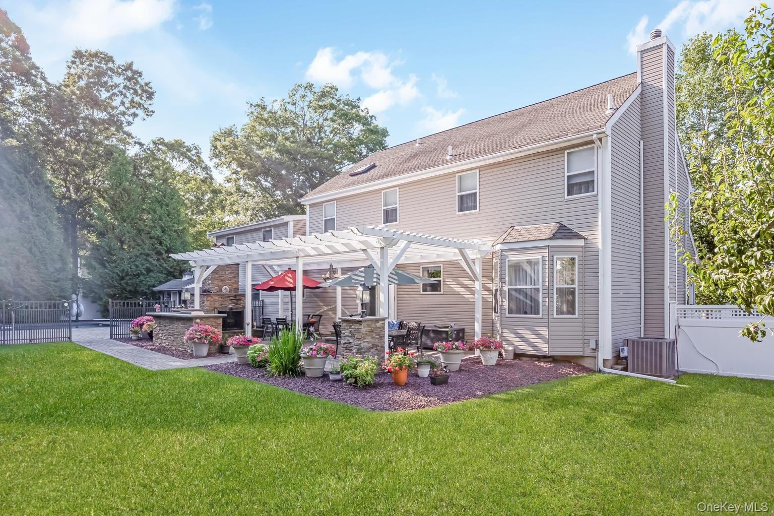 Expansive backyard featuring a manicured lawn, a stone patio with a white pergola, and an outdoor kitchen area with a built-in grill