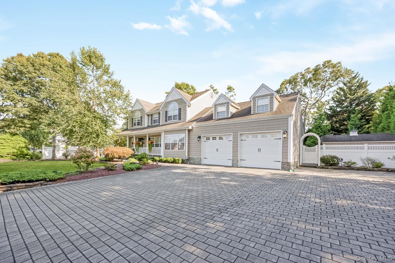 Paved driveway with a two-car garage, dormer windows, covered front porch, and an arched garden gate