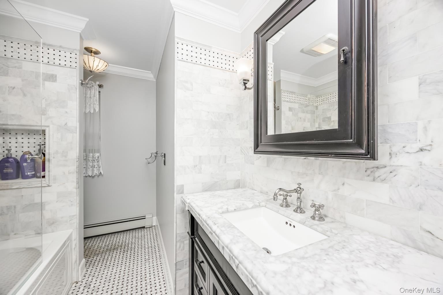 White marble tile walls, black framed mirror, white vanity sink, chrome faucet, and black and white patterned floor tile