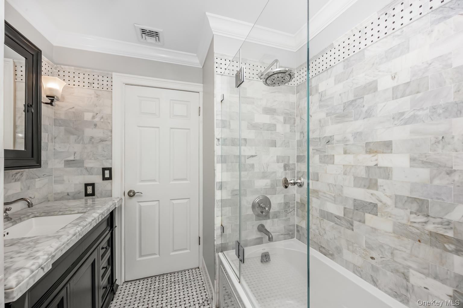 White subway tile shower surround with a rain shower head, glass shower enclosure, white bathtub, and mosaic tile flooring