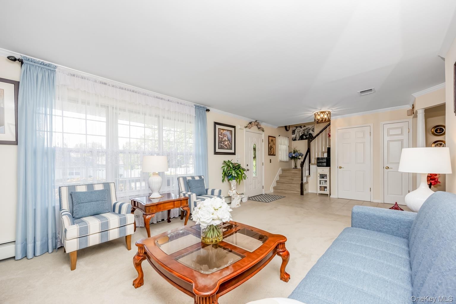 Spacious living area featuring expansive windows, neutral carpeting, and a staircase with dark wood handrail