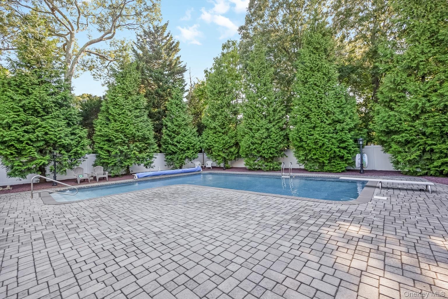Outdoor swimming pool with integrated steps, surrounded by a paver patio and a privacy fence